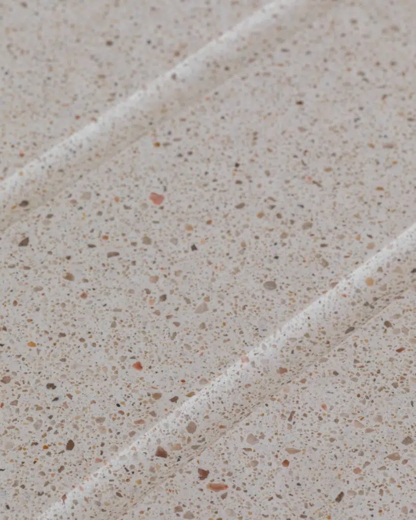 Gros plan sur une surface en terrazzo beige parsemée d’éclats de pierre, avec des rainures en relief