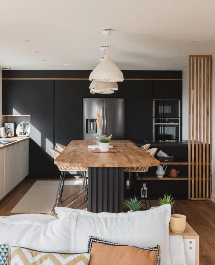 Cuisine ouverte avec table XXL en guise d’îlot, en FENIX® noir et blanc et chêne lamellé